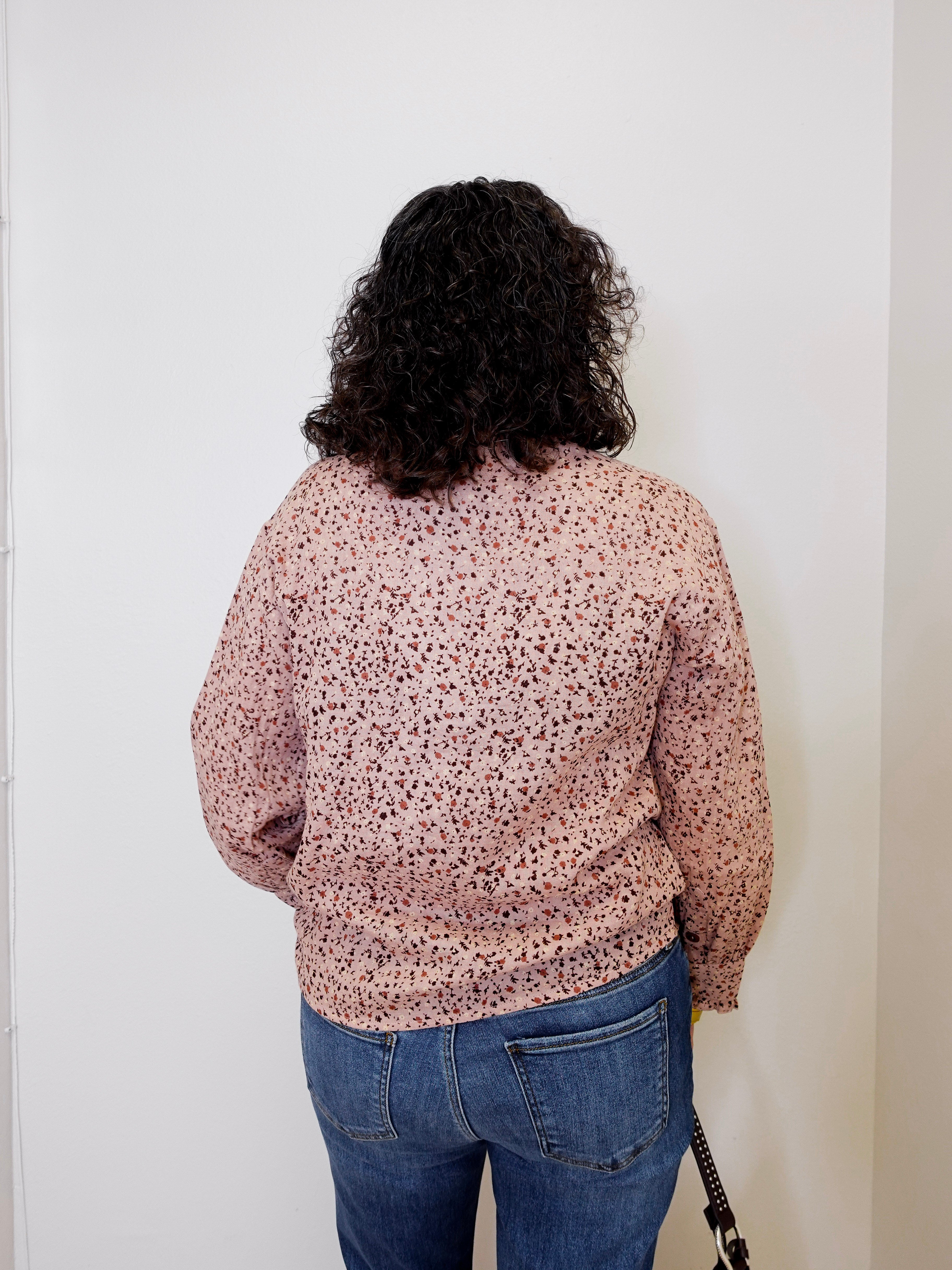 Person wearing a patterned shirt and jeans against a white wall