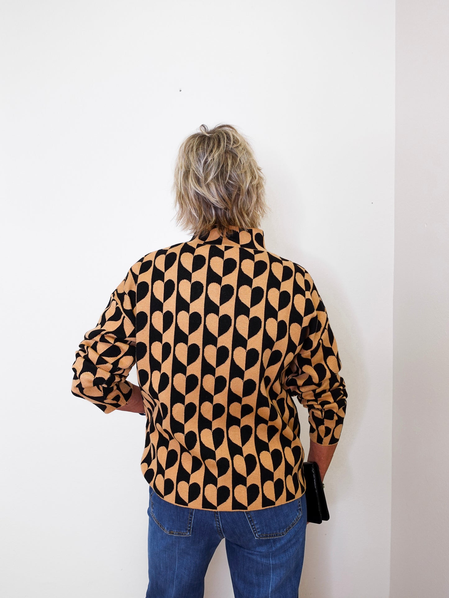A woman modeling a mock neck heart pattern sweater in front of a white wall.