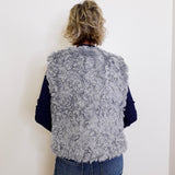 Person wearing a gray fluffy vest against a white background