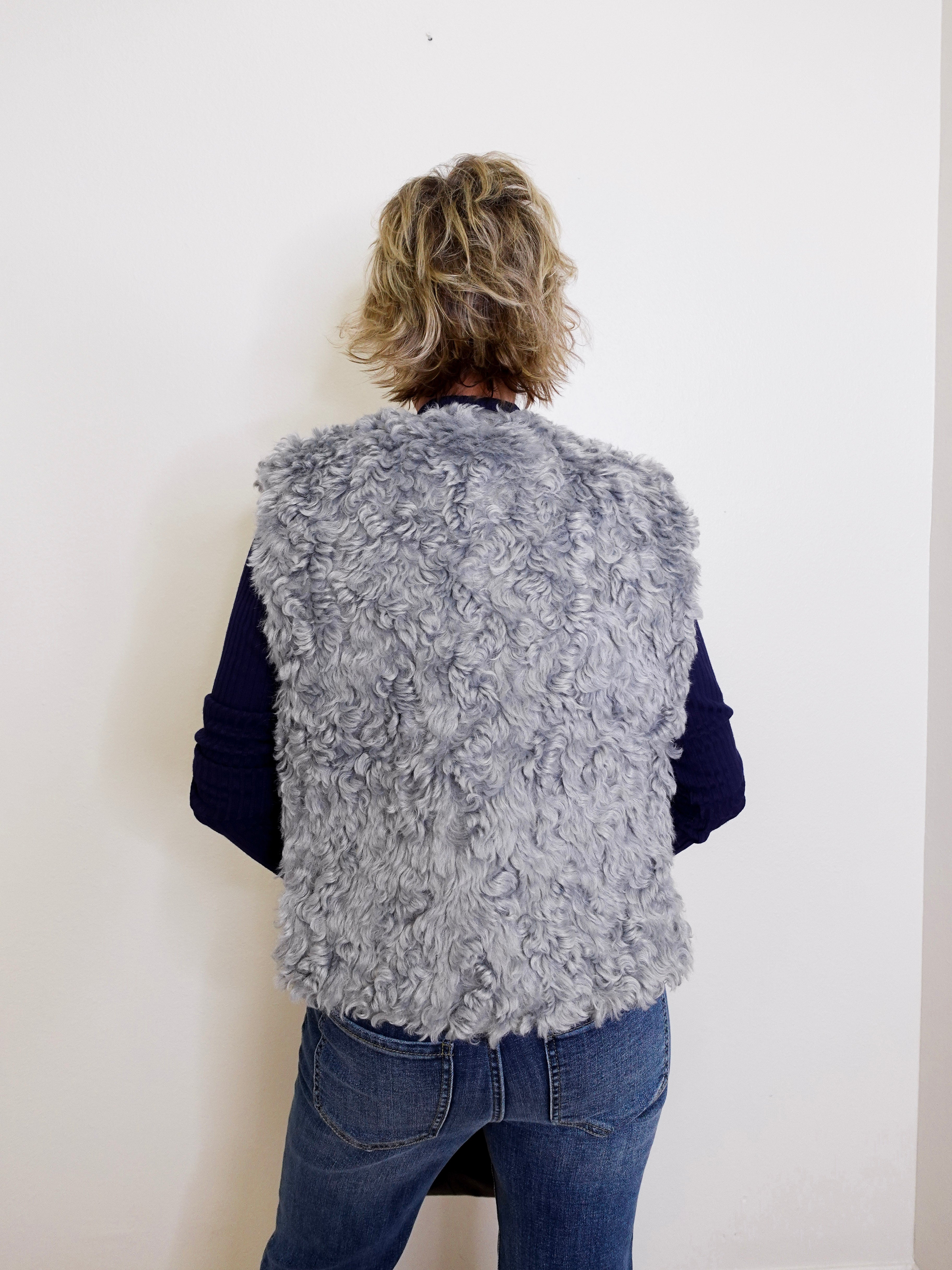 Person wearing a gray fluffy vest against a white background