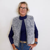 Person wearing a gray vest over a blue shirt with a white background