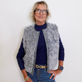 Person wearing a gray fur vest over a blue sweater and jeans against a white background