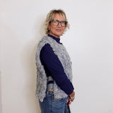 Woman wearing a blue sweater and gray vest against a white wall