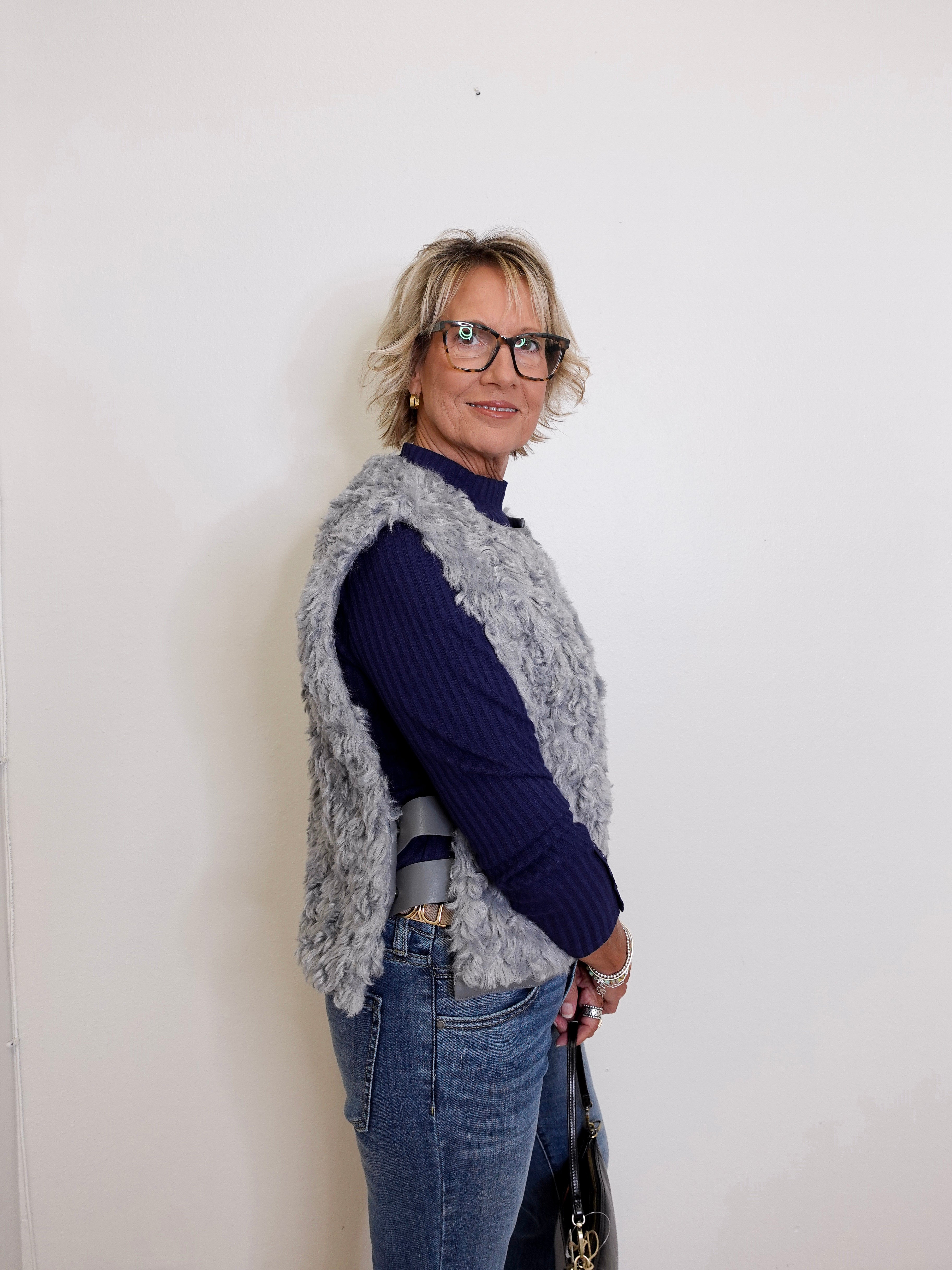 Woman wearing a blue sweater and gray vest against a white wall