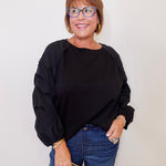 Woman wearing a black top and blue jeans, holding a clutch against a plain background