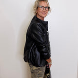 Person wearing a black jacket and camouflage pants against a white wall