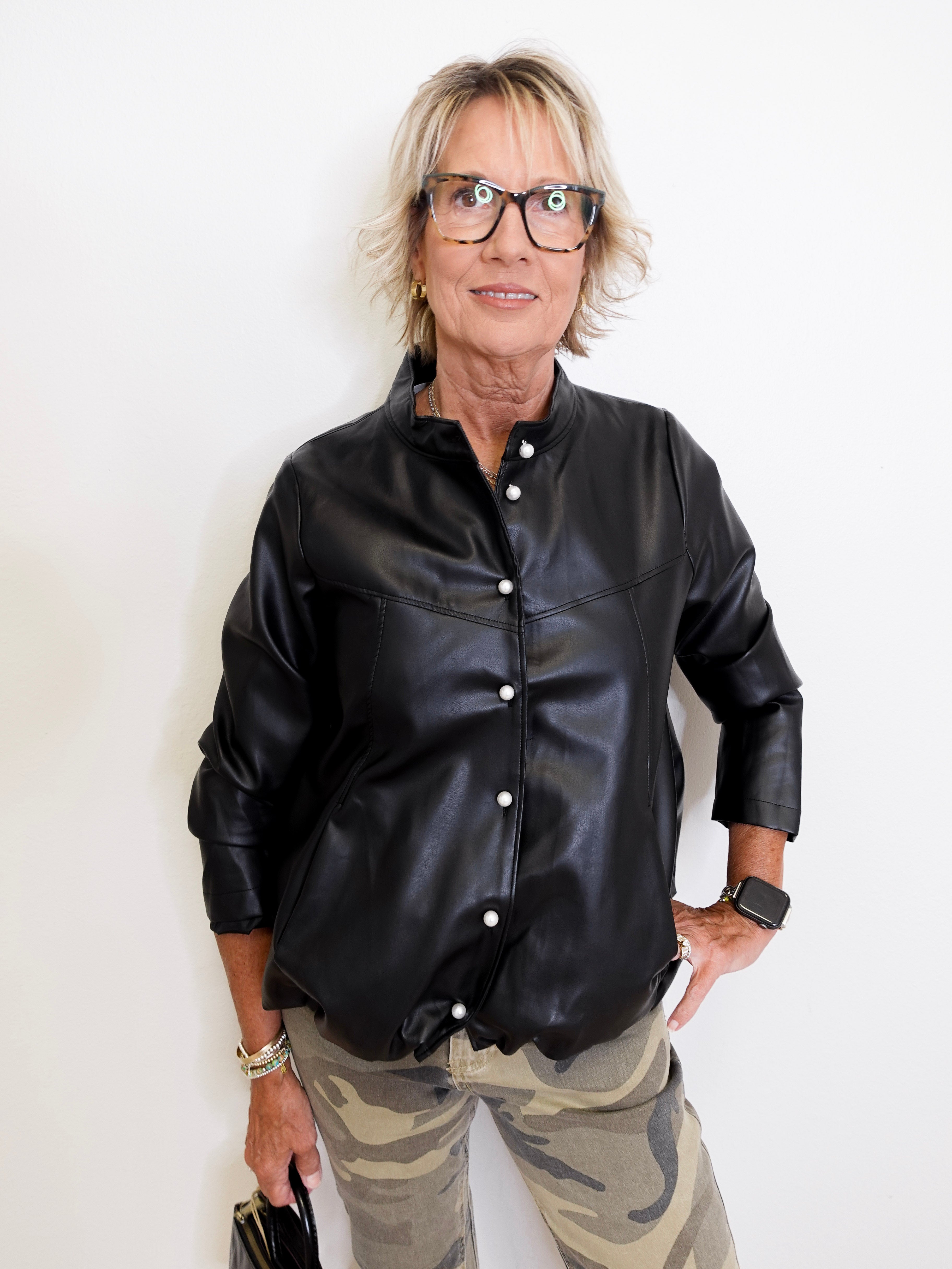 Person wearing a black leather jacket and camouflage pants against a white background