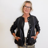 Person wearing a black leather bomber jacket, white shirt, and camouflage pants against a white background