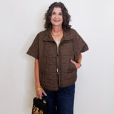 Woman wearing a brown vest and holding a black handbag with gold accents against a white background