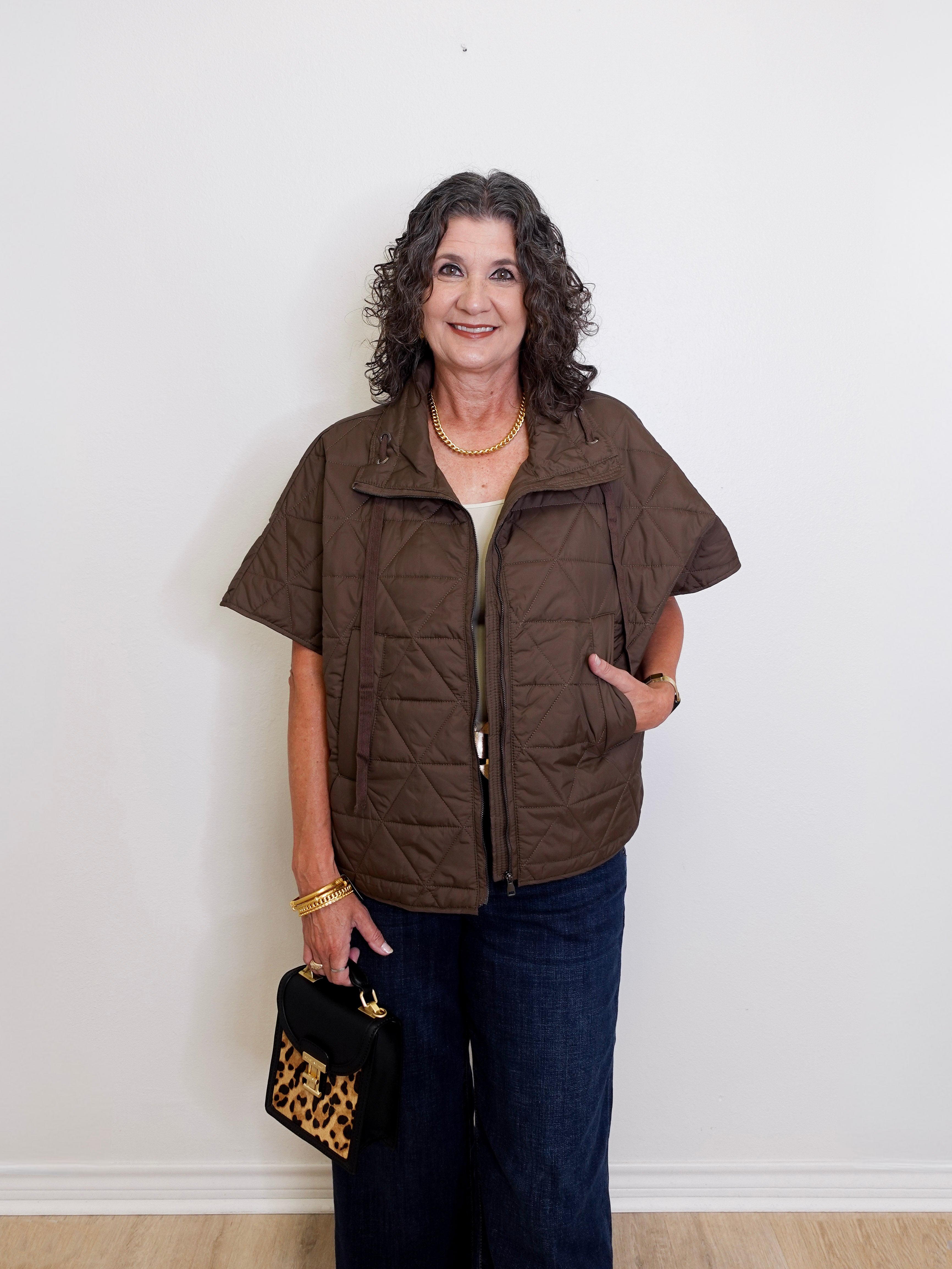 Woman wearing a brown vest and holding a black handbag with gold accents against a white background