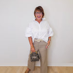 Woman wearing a white shirt, beige pants, and brown shoes against a white wall.