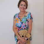 Woman in a colorful floral dress holding a teddy bear against a plain background