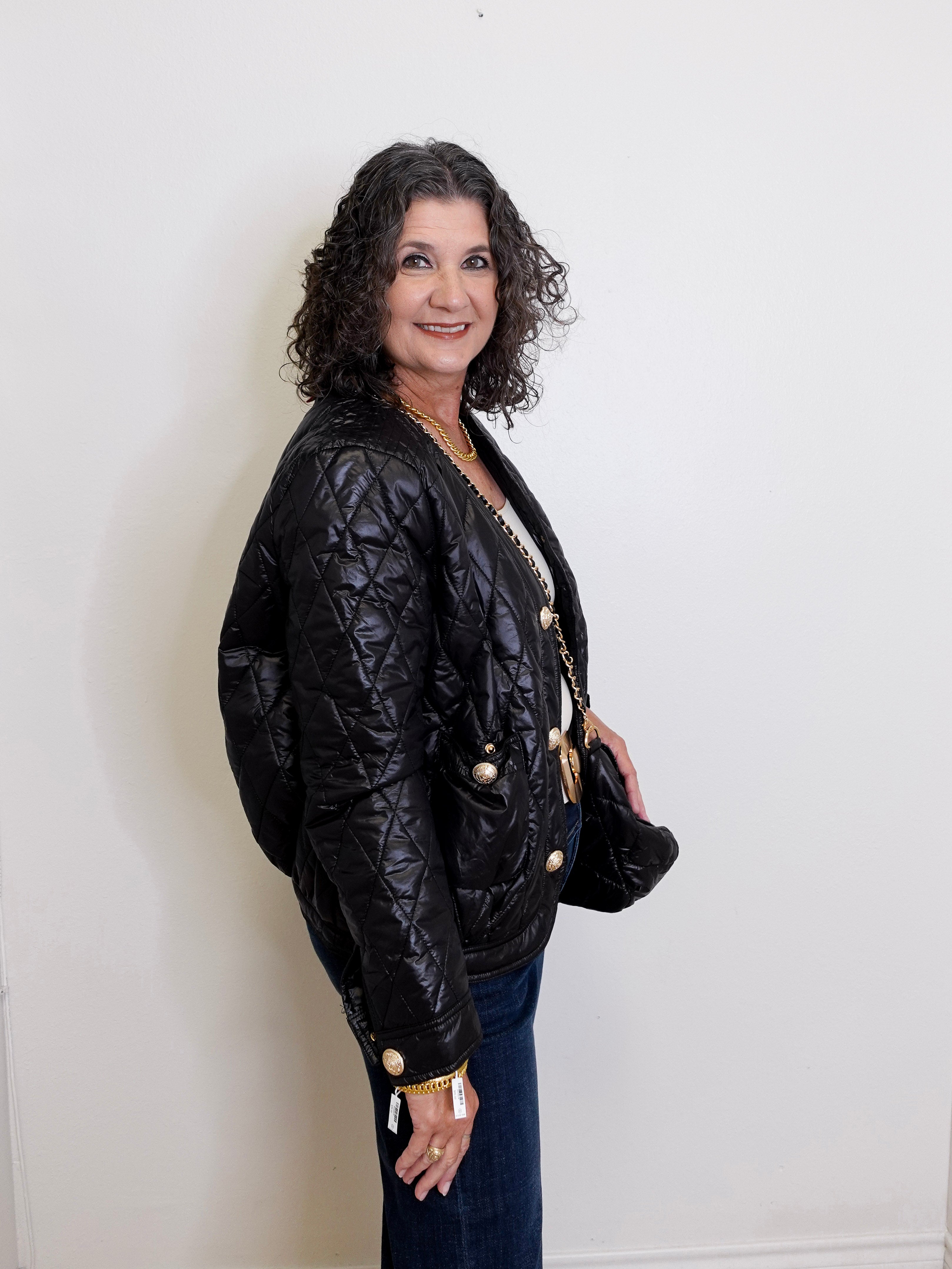 Woman wearing a black quilted jacket against a white wall