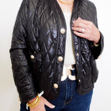 Person wearing a black quilted jacket with gold buttons on a white background