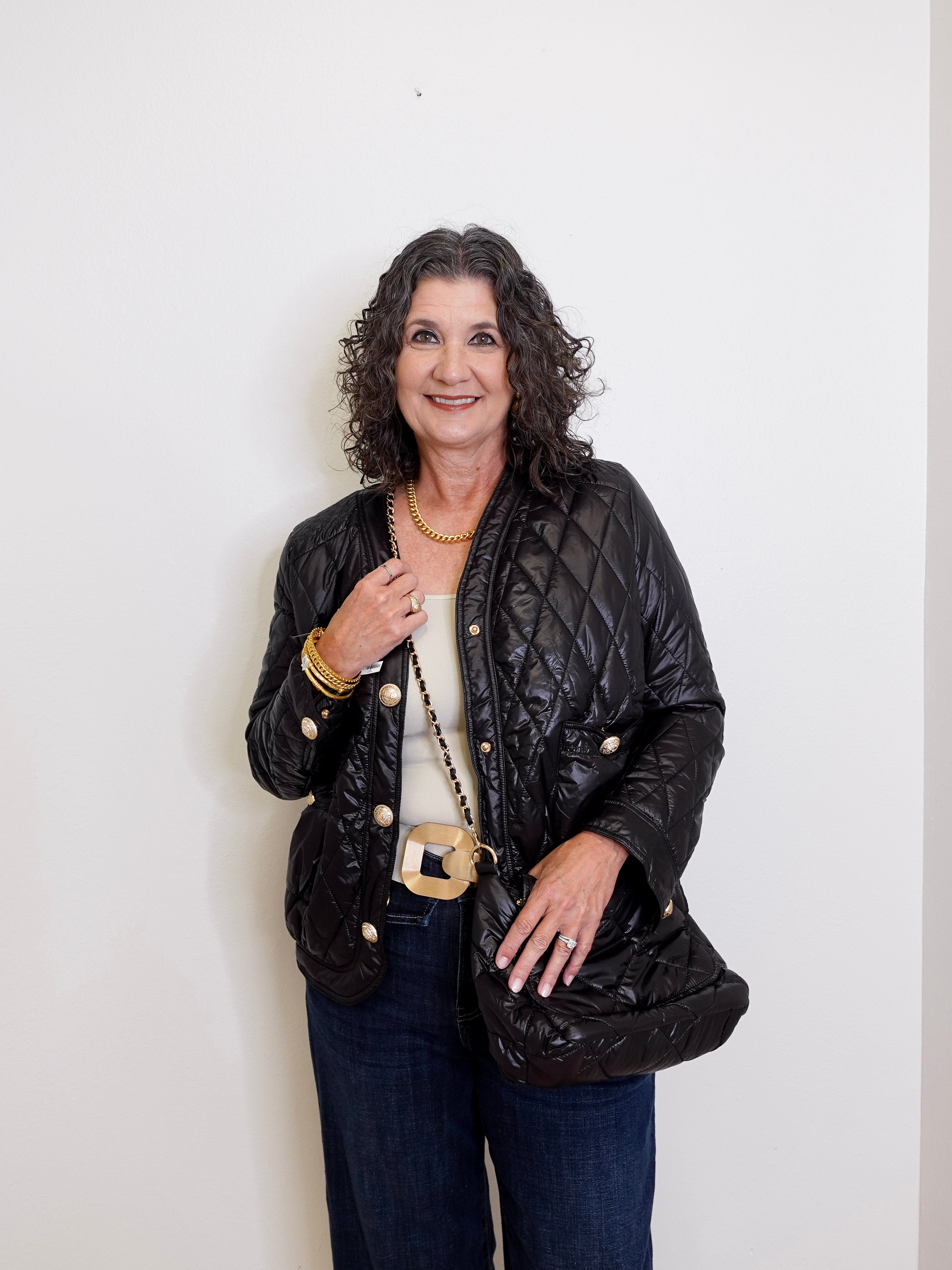 Woman wearing a black quilted jacket with gold buttons against a white background