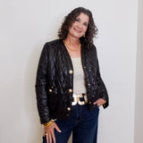 Woman wearing a black quilted jacket with gold buttons against a white background