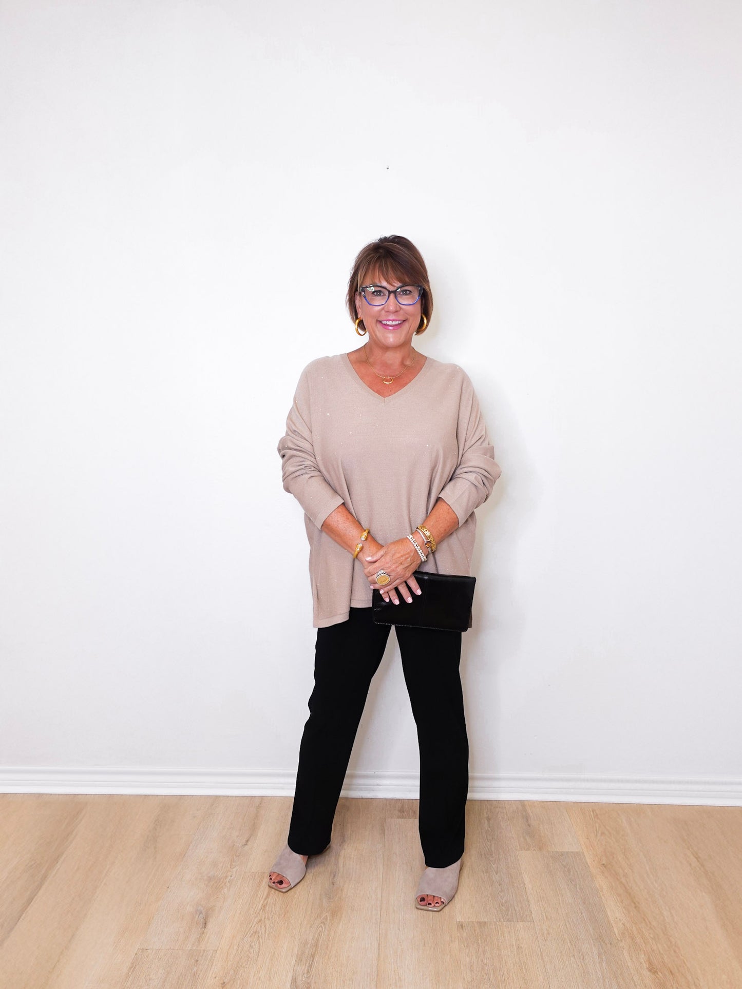 A woman wearing a v-neck jewel embellished sweater and black pants in front of a white wall.