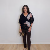 Woman wearing a black floral blouse and black pants against a white wall.