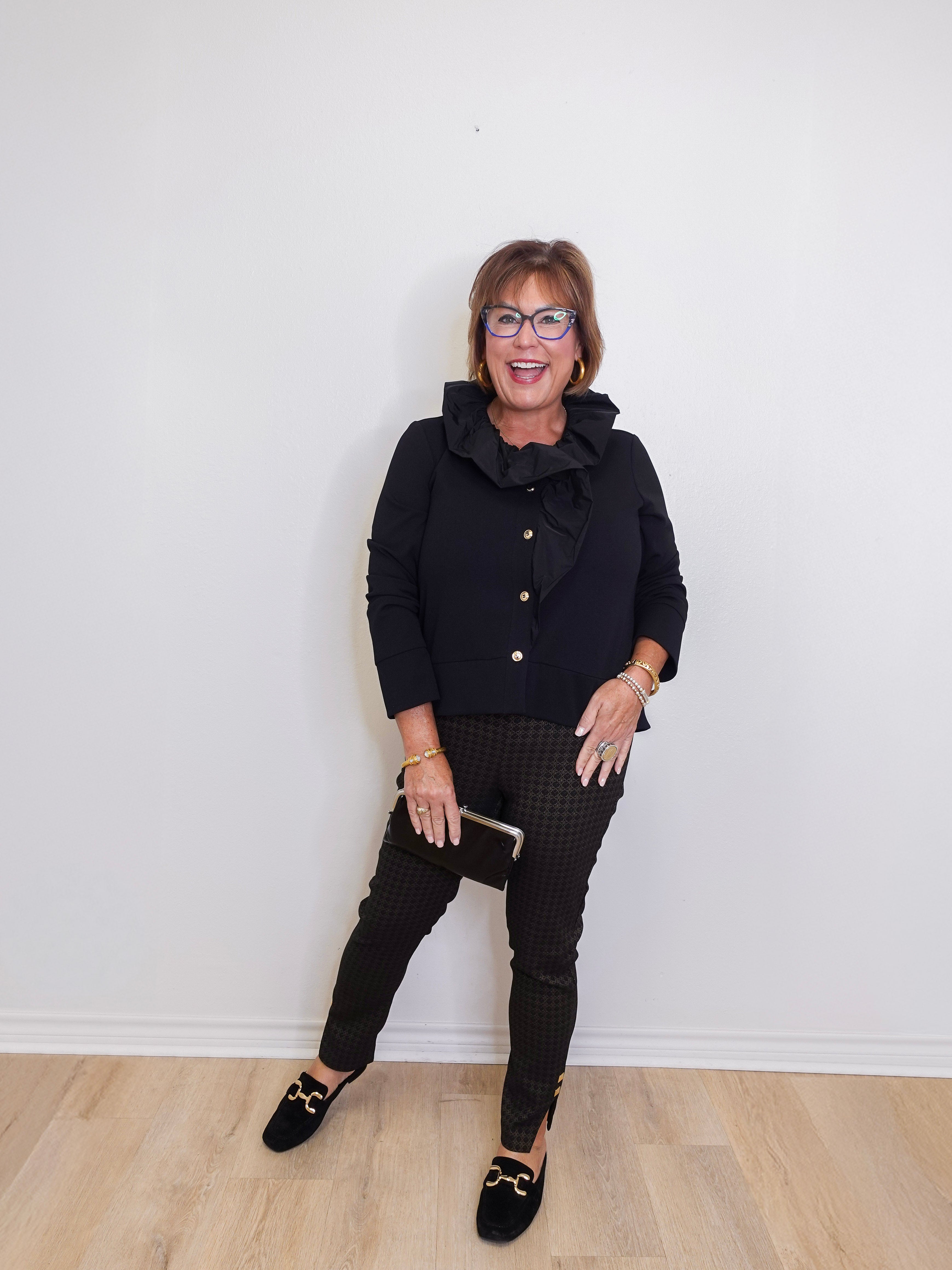 Woman wearing a black jacket and pants against a white wall