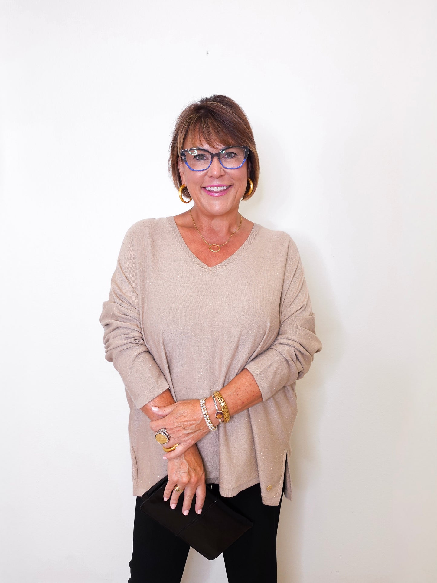 A women wearing a v-neck jewel embellished sweater in front of a white wall.