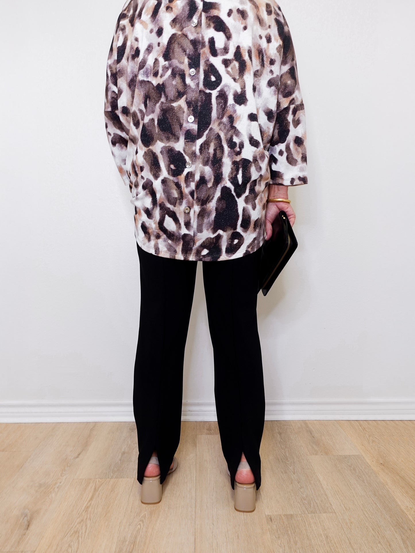 Person wearing a leopard print top and black pants against a white wall.