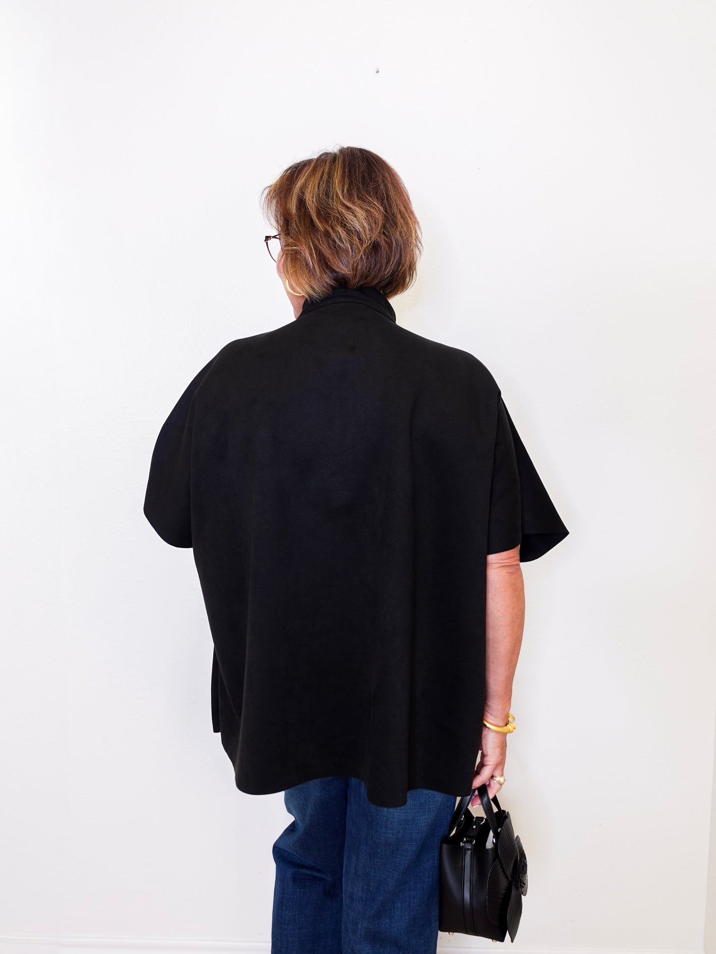 Person wearing a black cape and blue pants against a white wall