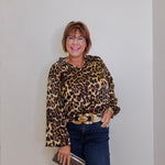 Person wearing a leopard print blouse and blue jeans against a plain background