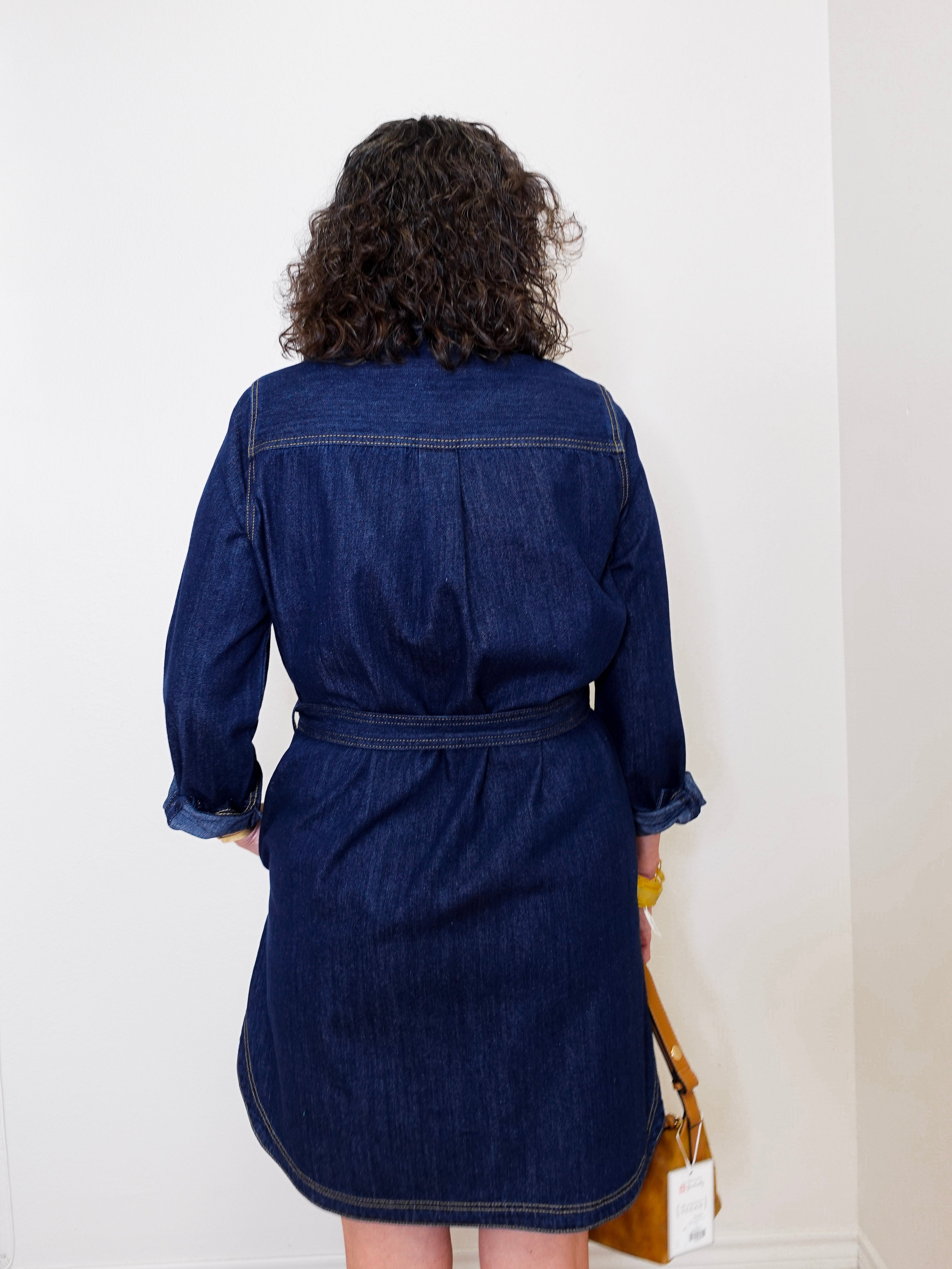 Person wearing a blue denim dress against a white wall