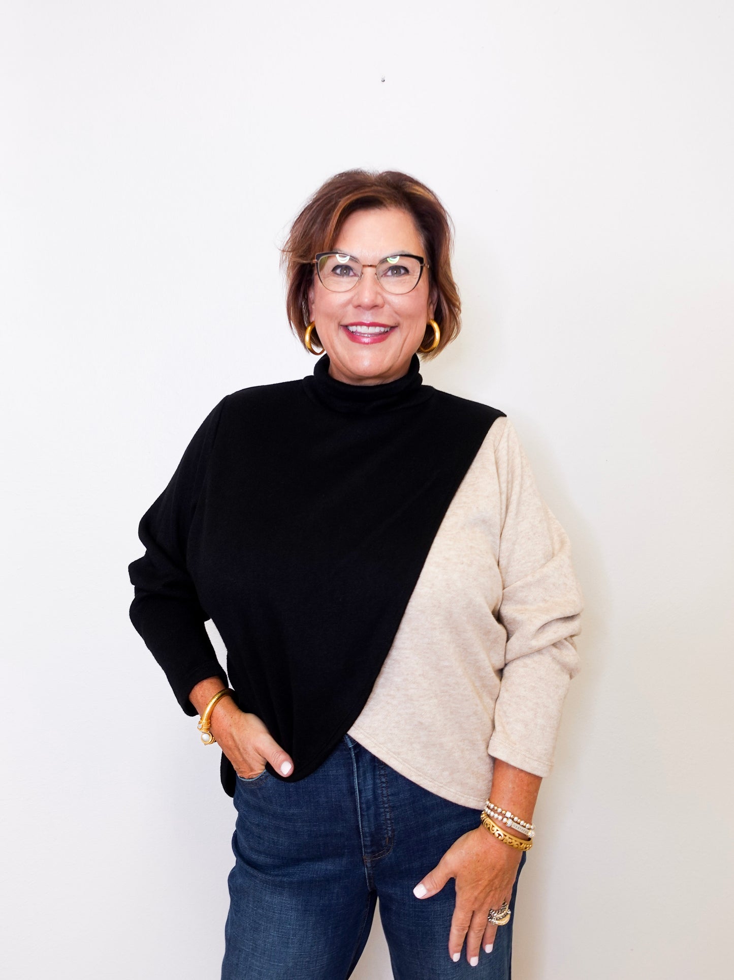 Woman wearing a black and beige sweater with blue jeans against a white background