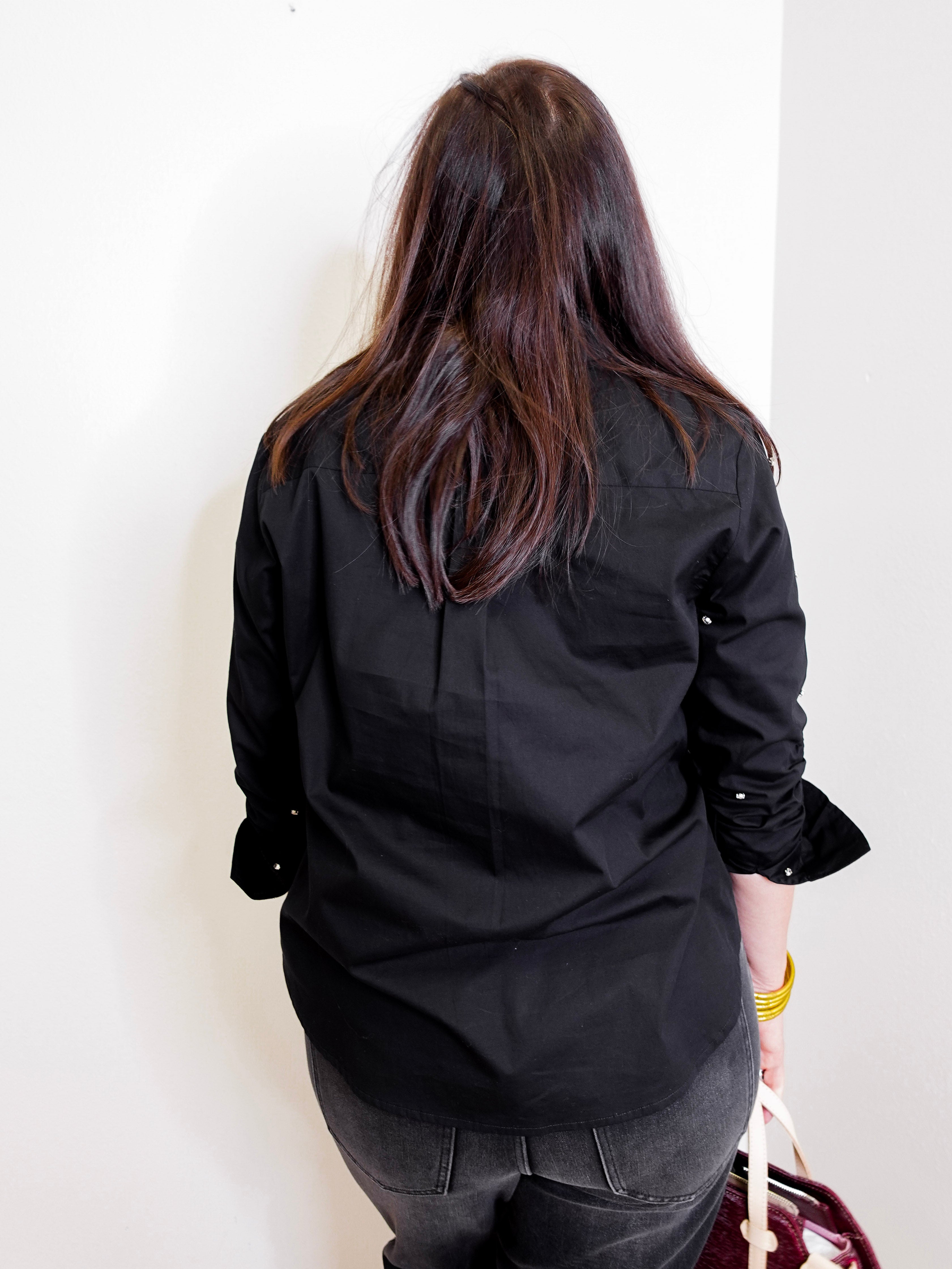 Person wearing a black top and pants against a white wall