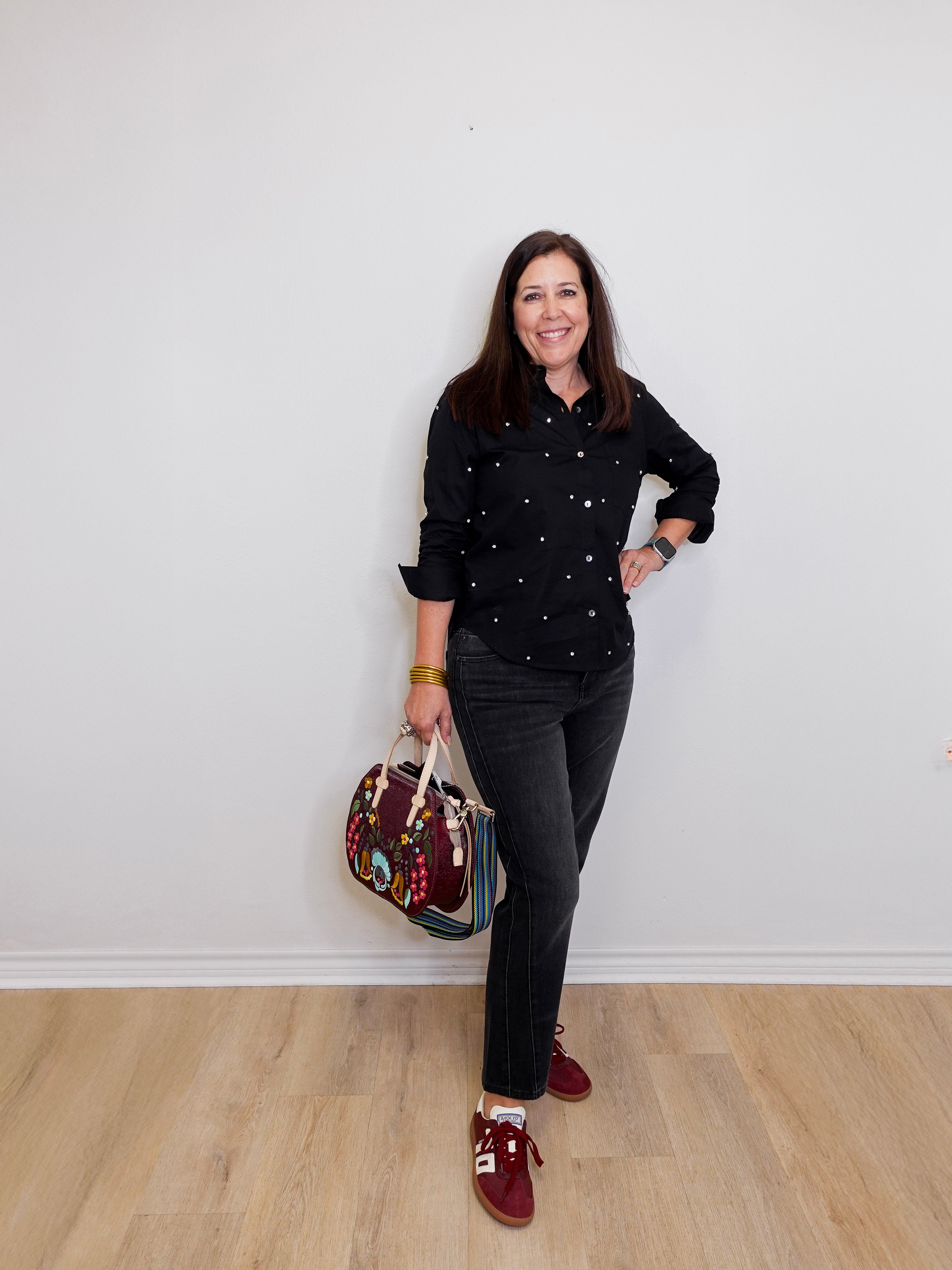 Woman in black shirt and jeans holding a colorful bag against a white wall.
