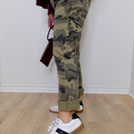 Person wearing camouflage pants and white sneakers on a wooden floor.