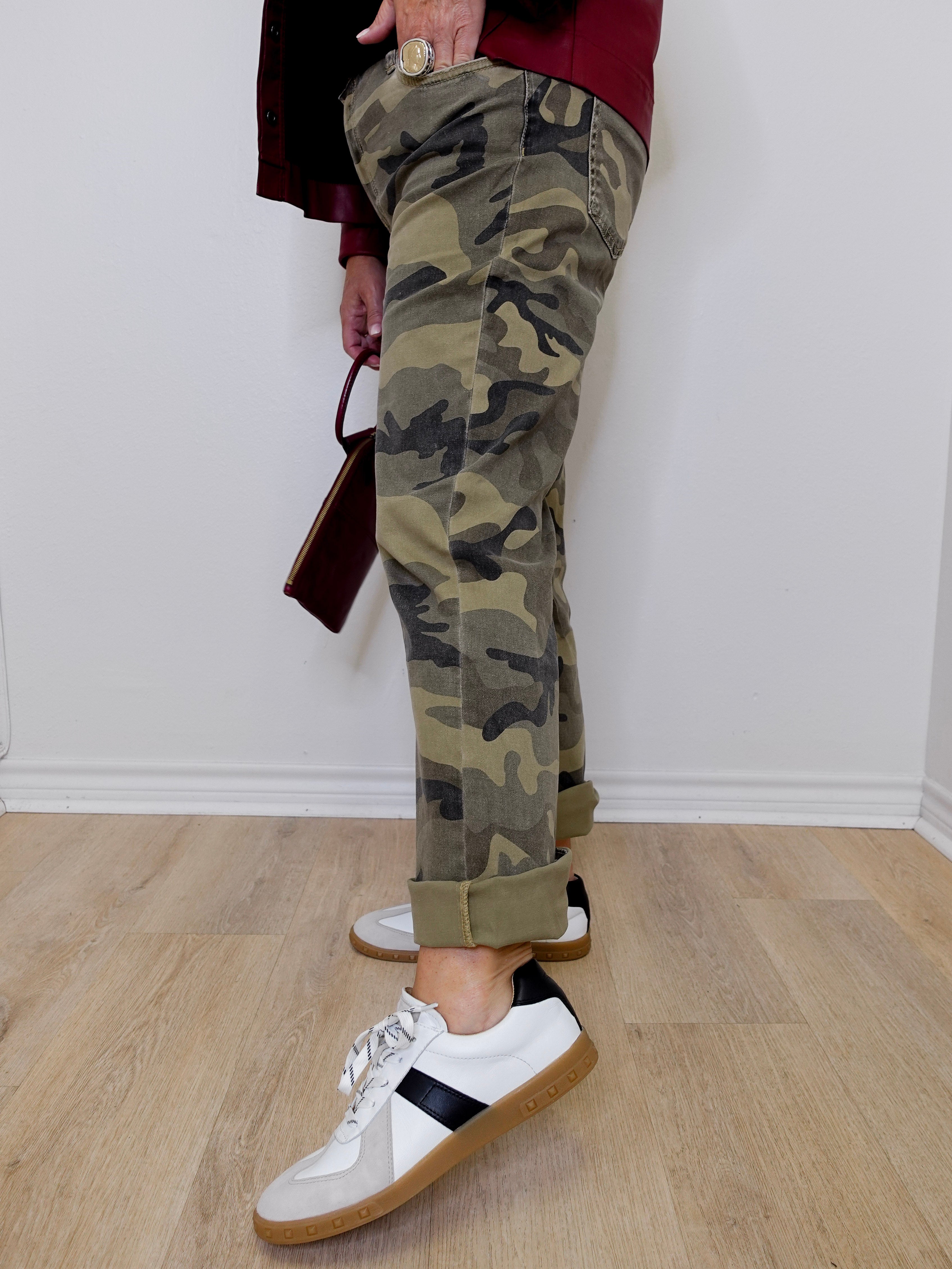 Person wearing camouflage pants and white sneakers on a wooden floor.