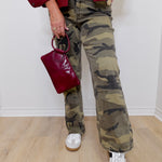 Person wearing camouflage pants, white sneakers, and a red jacket holding a matching red handbag.