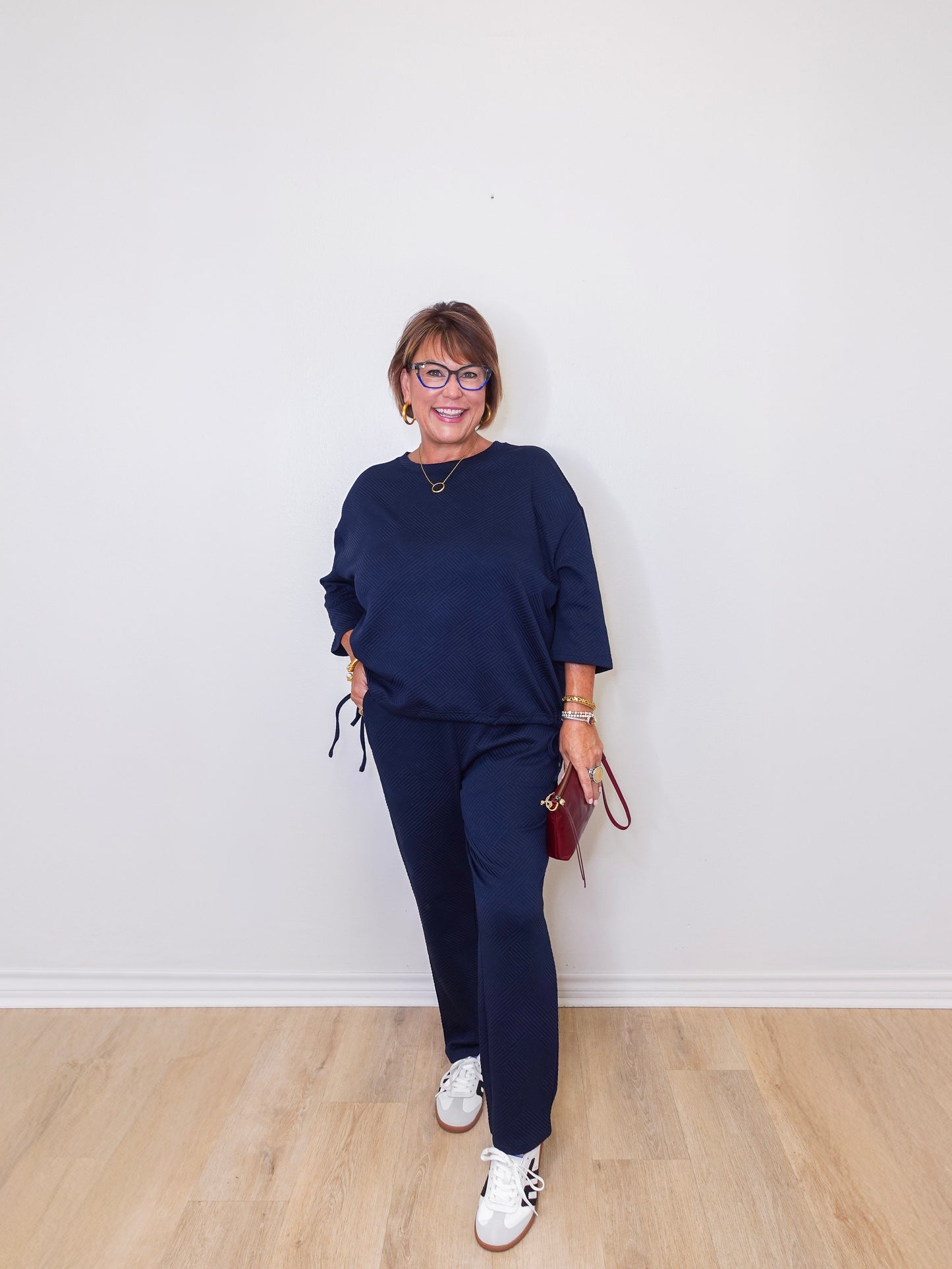 Person wearing a navy blue outfit with white sneakers against a white wall.