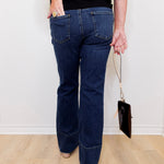 Person wearing blue jeans and a black top, holding a small black handbag on a light wooden floor.