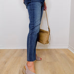 Person wearing blue jeans and beige sandals holding a tan handbag indoors.