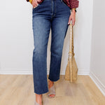 Person wearing blue jeans and a plaid shirt with a beige bag indoors.