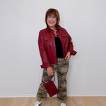 Woman wearing a red jacket, black top, camouflage pants, and white sneakers against a white wall.