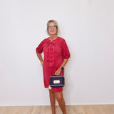 Woman in a red dress holding a small bag against a white wall
