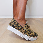 Leopard print sneakers with white soles worn indoors on a wooden floor.