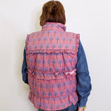 Person wearing a pink patterned vest over a blue shirt against a white background