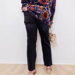 Person wearing a patterned top and black pants with a white background