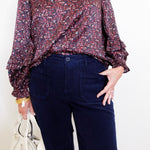 Person wearing a patterned blouse and dark pants with a white background