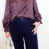Person wearing a patterned blouse and dark pants with a white background