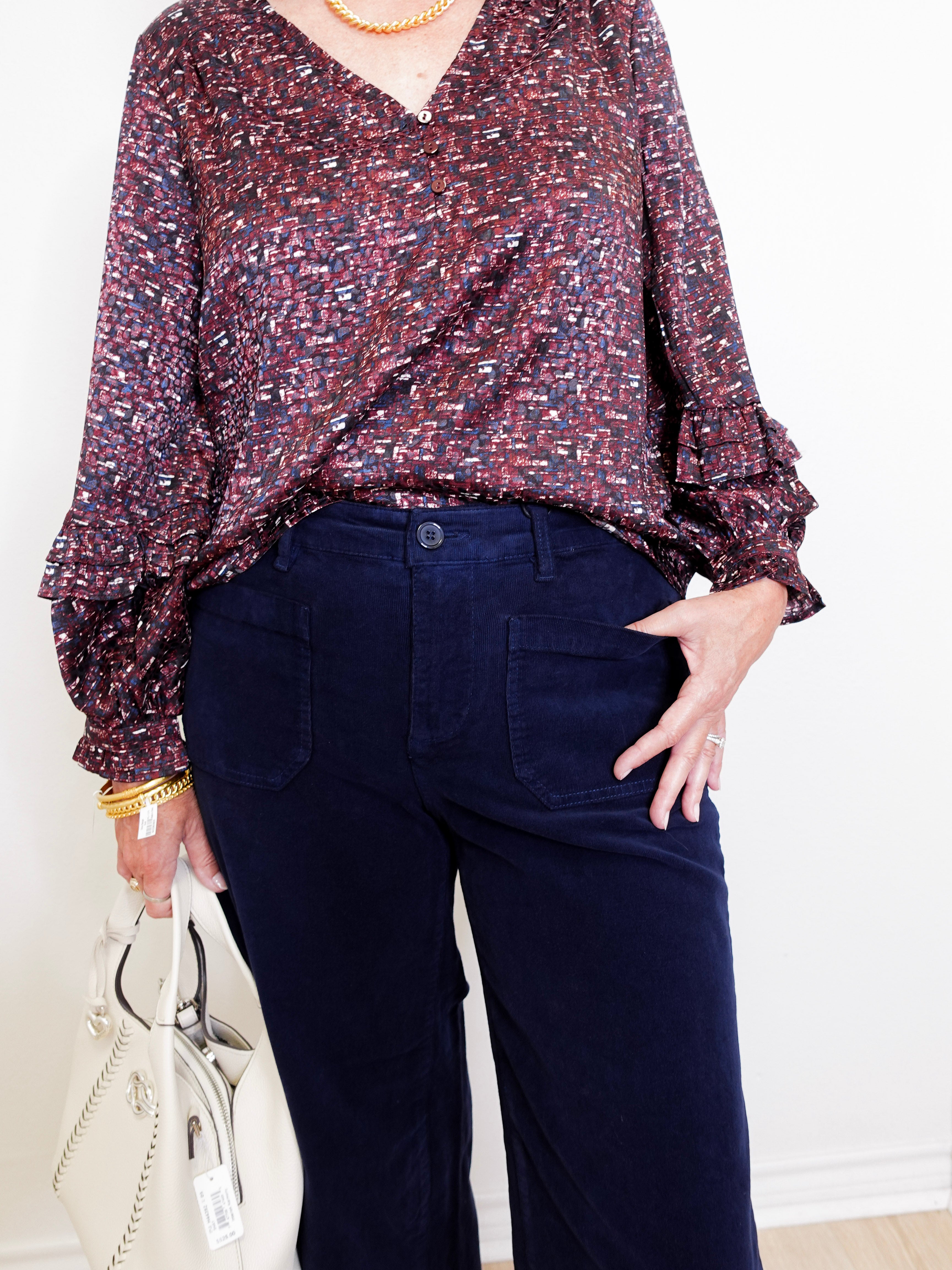 Person wearing a patterned blouse and dark pants with a white background