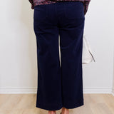 Person wearing navy blue pants with a patterned top on a white background