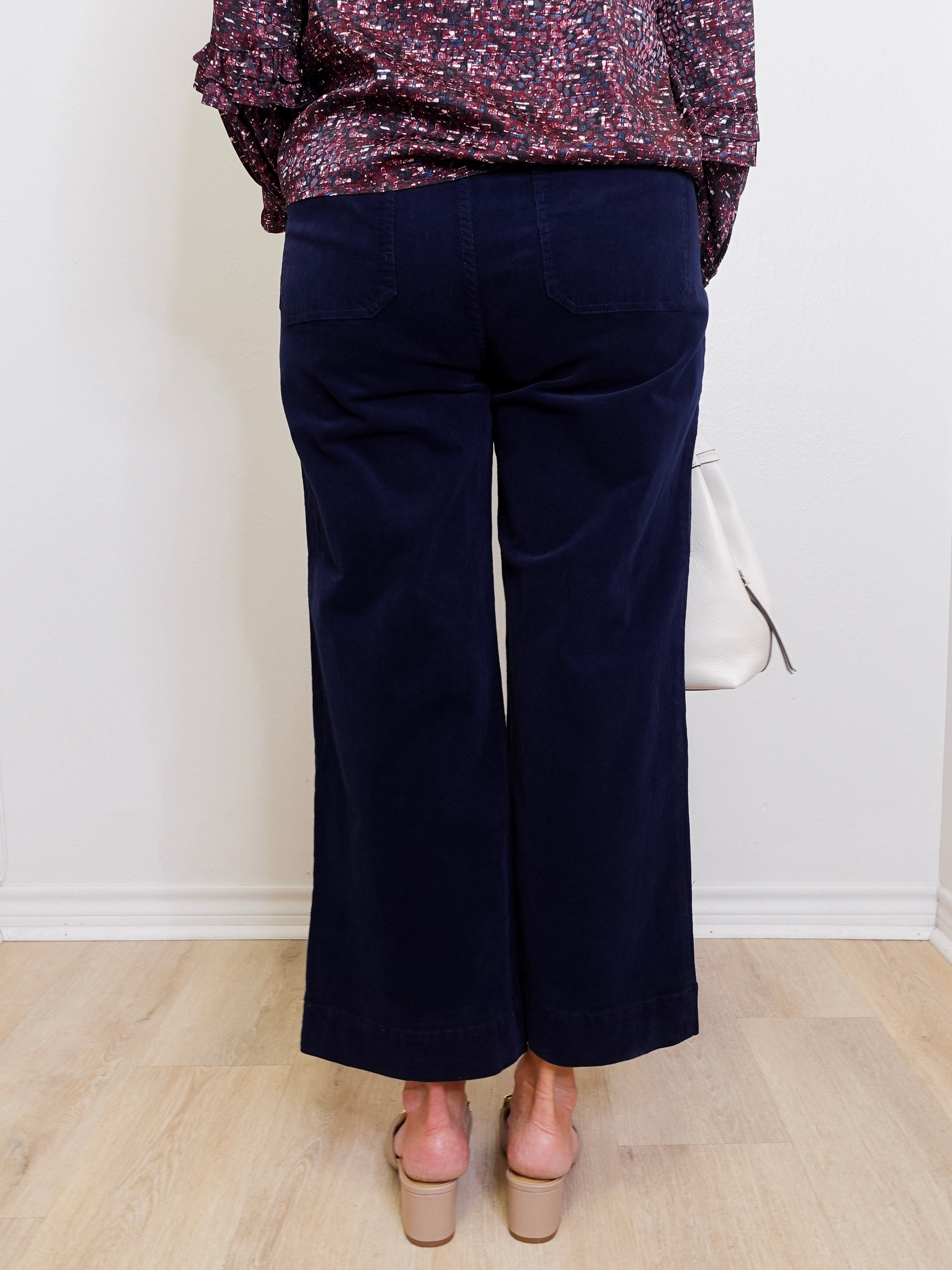 Person wearing navy blue pants with a patterned top on a white background