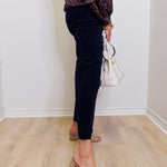 Person wearing navy pants and a patterned top, standing against a white wall.