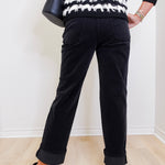 Person wearing a black and white striped sweater and black pants against a white wall.